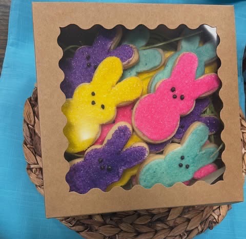 A bakery box with a window lid holding brightly frosted bunny-shaped sugar cookies in yellow, pink, purple and teal.