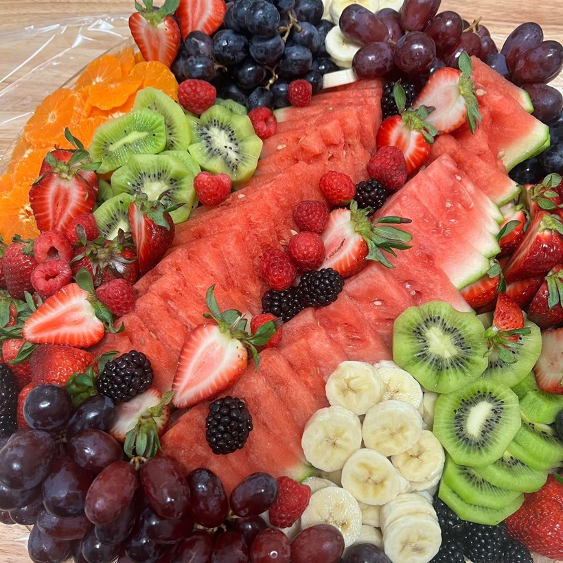 A fresh fruit tray with a long watermelon slice down the center, ringed by kiwi, strawberries, raspberries, blackberries, grapes and bananas.
