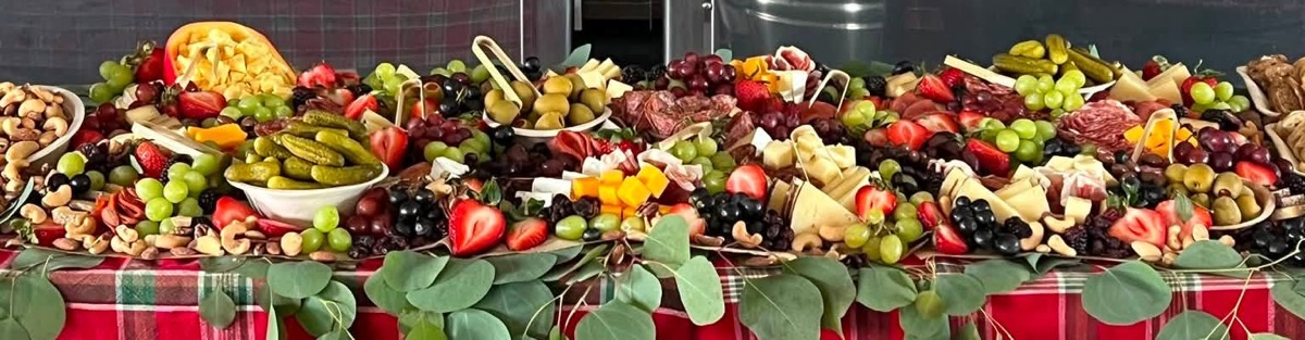 A long grazing table running the length of a room, heaped with meats, cheeses, fruit and nuts and trimmed with eucalyptus garland over a red plaid cloth.