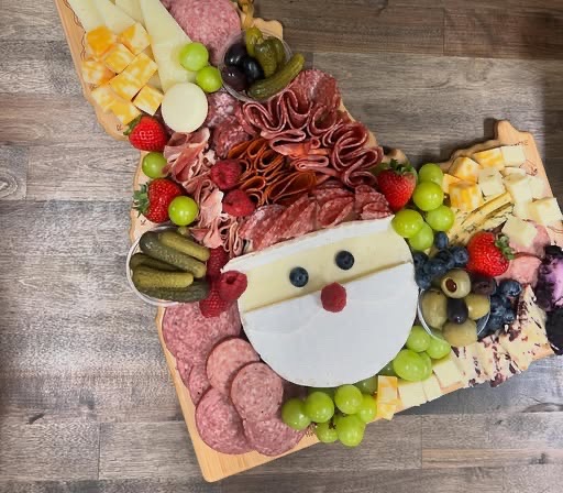 A large custom charcuterie board arranged with cheeses, salami, prosciutto, grapes, strawberries, olives and pickles on a wooden board.
